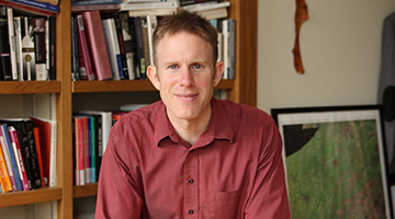 Professor and Author Nico Slate facing the camera, smiling and wearing a burgundy buttondown shirt.